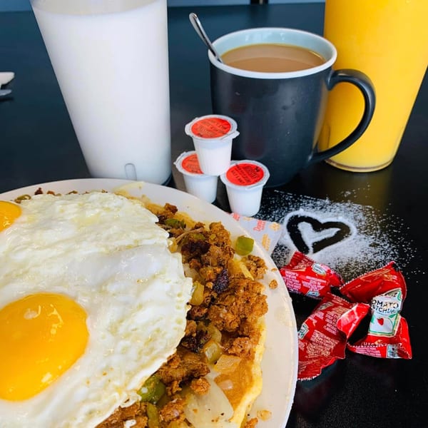 An American breakfast with fried eggs, chorizo, and hash browns, alongside coffee, milk, and orange juice.