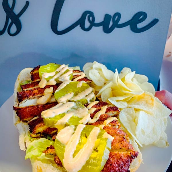 A crispy chicken sandwich with pickles, lettuce, and sauce, served with potato chips.