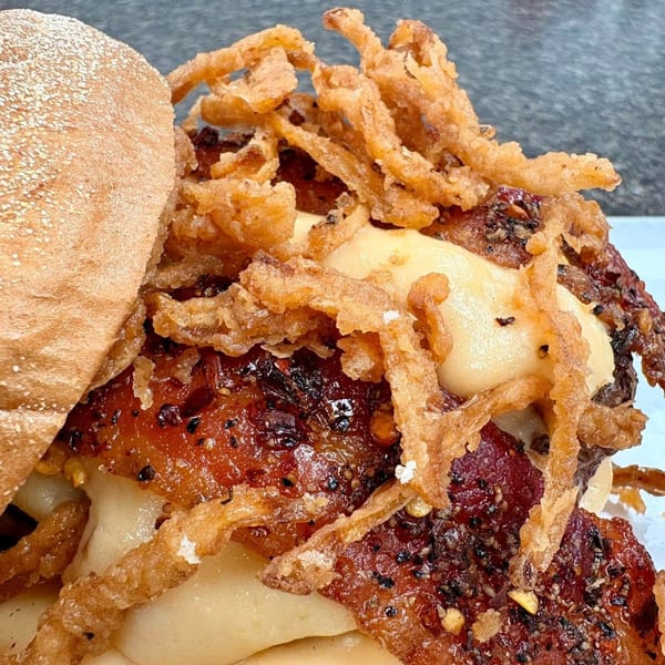 Close-up of a burger with crispy fried onions, melted cheese, and a toasted bun.