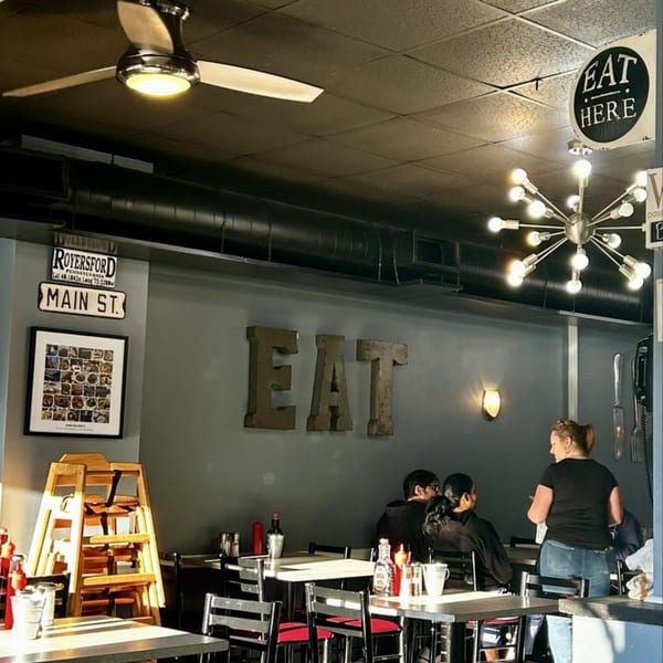 Interior of Annamarie's Place with customers, tables, and a large "EAT" sign on the wall.