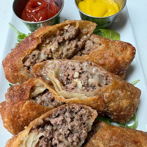 Cheesesteak egg rolls, cut open to show the meat and cheese filling, served with ketchup and mustard.