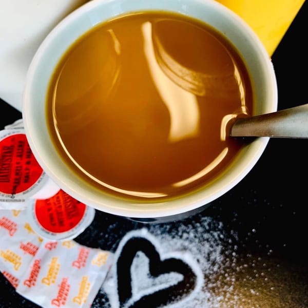 Overhead view of a coffee cup with a spoon, creamer, sugar packets, and a sugar heart.