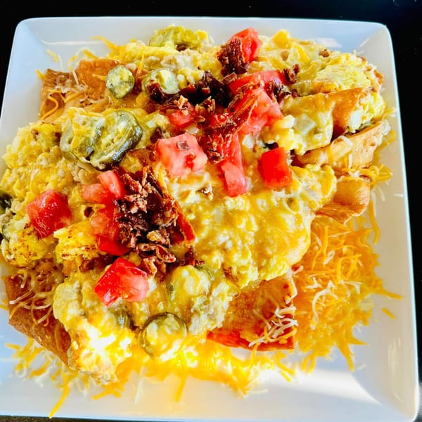 A plate of breakfast nachos with scrambled eggs, cheese, bacon, tomatoes, and jalapeños.
