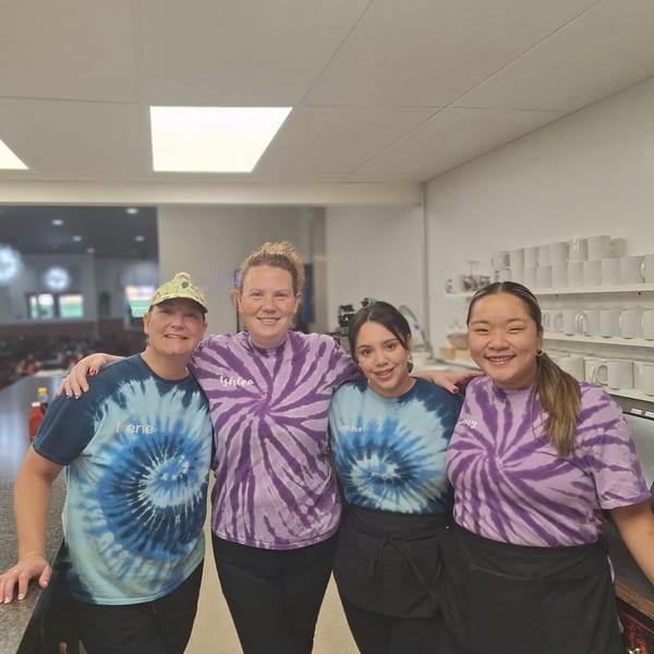 Four smiling women in tie-dye shirts stand together in a restaurant kitchen at Annamarie's Place.