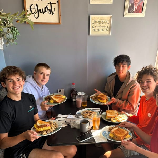 Five young men enjoying breakfast sandwiches and pancakes at Annamarie's Place.