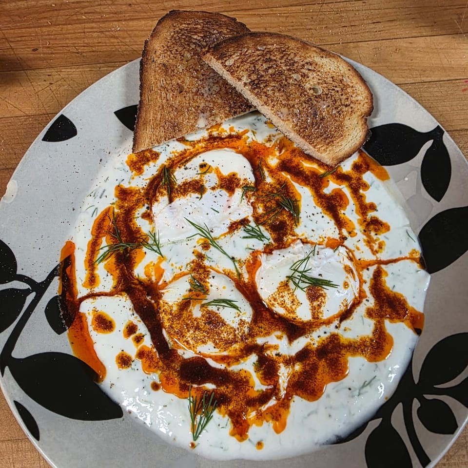 Annamarie's Place's poached eggs with yogurt, chili oil, dill, and toast on a decorative plate.